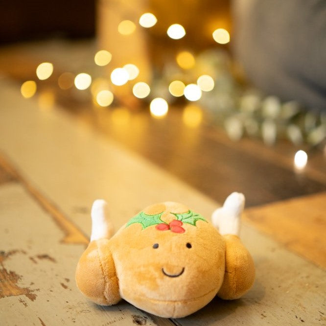 Plush roast turkey dog toy with candles on a wooden surface with blurred lights in the background